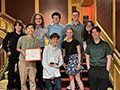  students pose on a staircase with a glass trophy